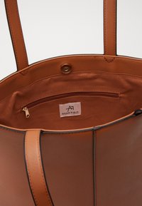 Borsa a tracolla marrone realizzata in materiale liscio e strutturato. Presenta una tasca interna con zip, etichetta del marchio e due manici lunghi.
