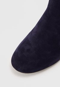 Bottine en suédine bleu marine profond, avec un bout arrondi et une texture lisse, dotée d'une semelle plate basse et de détails de couture discrets.