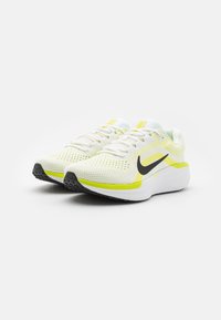 Des chaussures de course légères avec une tige en maille blanche, accentuées de jaune et d'un swoosh noir de Nike, offrant une semelle rembourrée et une adhérence texturée.