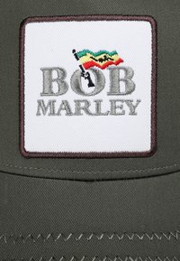 Zielona czapka z prostokątną białą wstawką, na której szaro haftowane jest "BOB MARLEY", a nad grafiką czarnej broni znajduje się kolorowy wzór flagi.