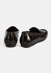 Schwarze Lederloafers mit einem krokodilgeprägten Muster, flacher Sohle, runder Zehenform und einem leicht erhöhten Absatz hinten.