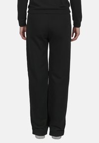 Pantalones de chándal de algodón negros con un corte relajado, que presentan una textura suave y una cinturilla elástica, diseñados para ofrecer comodidad y facilidad de movimiento.