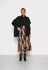 En svart oversized cardigan over en svart skjorte, kombinert med et beige skjørt med markante svarte tigerstriper. Svart ankelstøvler fullfører antrekket.