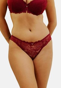 Ensemble en dentelle bordeaux composé d'un soutien-gorge et d'un string, avec des motifs floraux, des bords festonnés et un subtil accent en forme de cœur doré au centre devant.