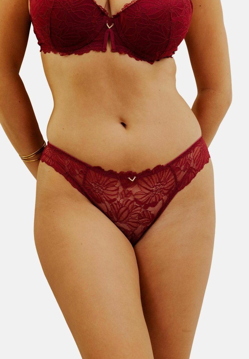 Ensemble en dentelle bordeaux composé d'un soutien-gorge et d'un string, avec des motifs floraux, des bords festonnés et un subtil accent en forme de cœur doré au centre devant.
