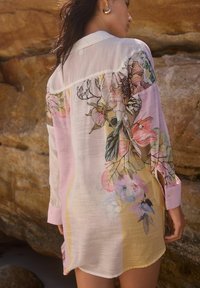 Camicia leggera e trasparente con motivi floreali in rosa pastello, giallo e verde. Maniche lunghe e polsini abbottonati, vestibilità rilassata.