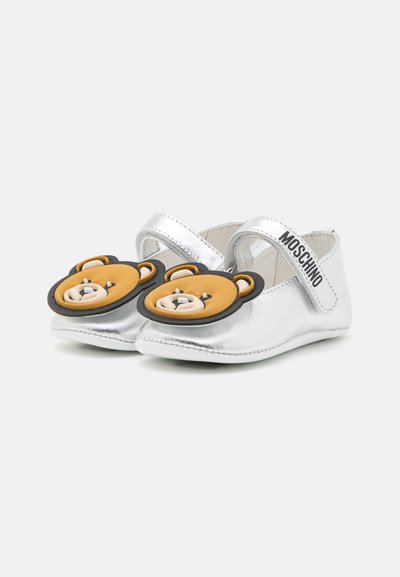 Zapatos infantiles metálicos plateados con adornos en forma de oso en la puntera y correa ajustable. Textura suave y forma redondeada.