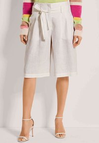 Witte linnen culottes met een gestrikte tailleband, met brede benen die onder de knie vallend zijn. Gecombineerd met strap-achtige, naaktkleurige open hakken.