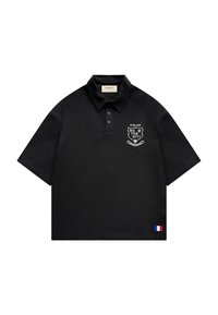 Polo noir à manches courtes avec col boutonné, écusson blanc « Atelier Reternity » sur la poitrine, et petit drapeau français près de l'ourlet.