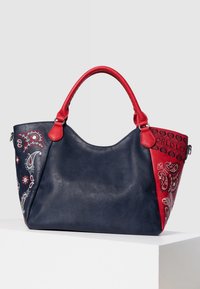 Skórzana torba na ramię o granatowym korpusie i czerwonych bokach. Posiada haftowane wzory paisley oraz napis "ŚWIATOWA MIŁOŚĆ" z jednej strony. Wytrzymałe uchwyty.