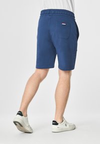 Pantaloni corti in cotone blu con cintura elastica, tasche laterali e una tasca sul retro con un piccolo etichetta del logo. Tessuto liscio e vestibilità casual.