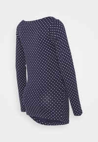 Laivastonsininen pitkähiha, jossa on valkoisia pilkkuja, esitelty takaa vaaleaa taustaa vasten.