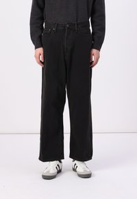 Svarte denimbukser med løs passform, med beltehemper og foran lommer. Båret med hvite sneakers og en mørk genser.