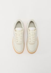 Sötétbarna texturált felületű vászon sneaker, lapos fűzőkkel és gumi talppal. Az oldalon világoskék díszítéssel.
