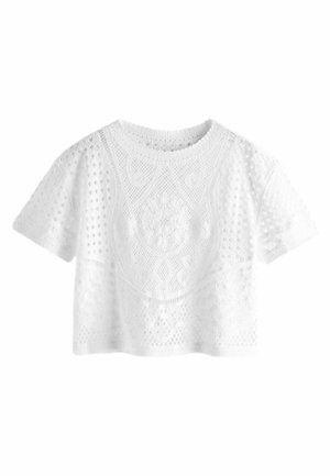 Haut blanc à manches courtes en crochet dentelle avec des motifs floraux et géométriques, col rond et coupe légèrement raccourcie sur fond blanc.