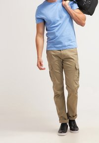 Camisa de manga corta azul claro, pantalones cargo color beige con bolsillos laterales y zapatillas negras. La persona lleva una bolsa negra al hombro.