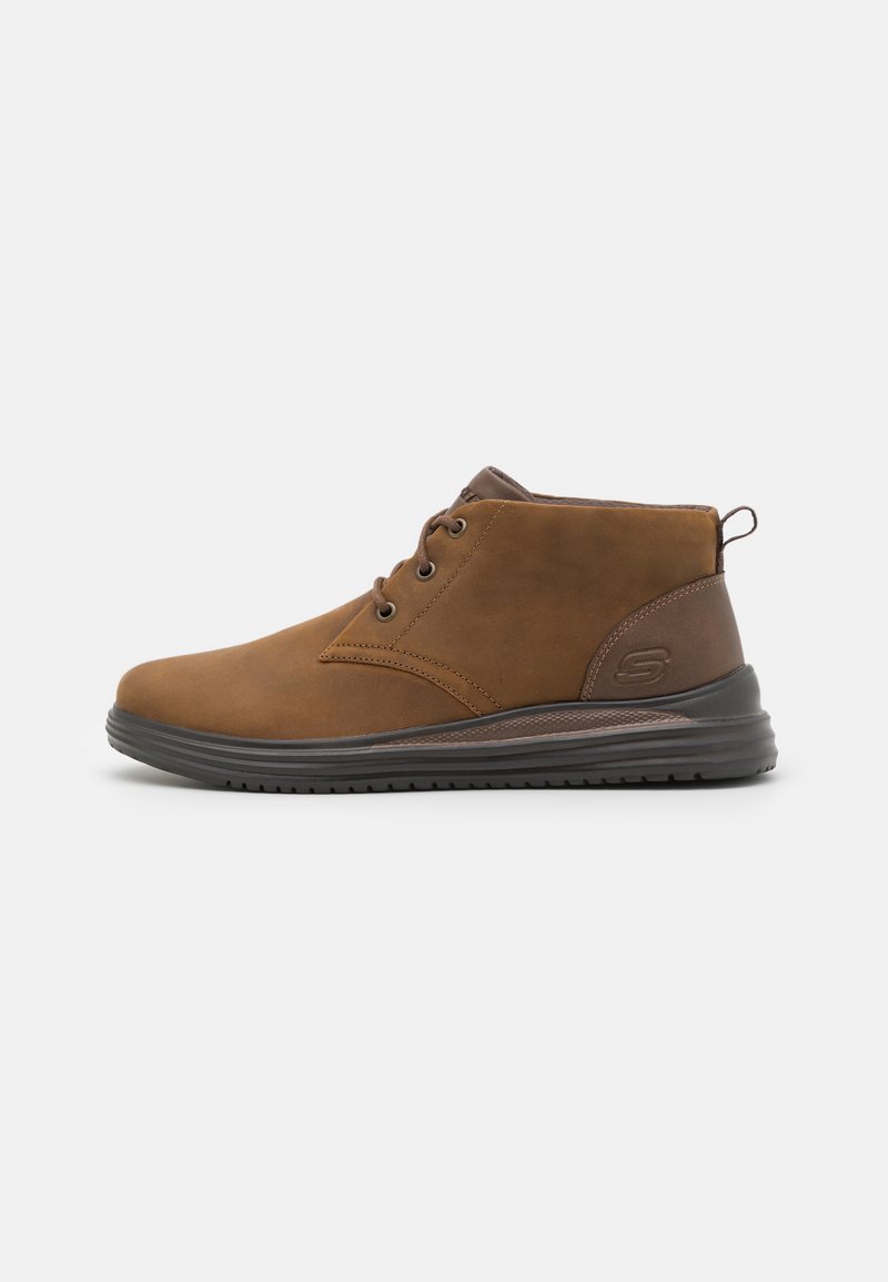 Botas de tobillo de ante marrón con punta redondeada, diseño de cordones con dos ojales y suela de goma texturizada. Con tacón de color marrón oscuro.