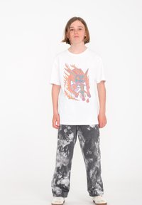 Camiseta blanca de algodón con un diseño gráfico colorido de un dragón, combinada con pantalones de pierna ancha gris tie-dye y zapatos beige.