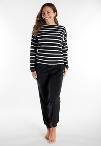 Schwarz-weiß gestreiftes Langarmoberteil mit Rundhalsausschnitt, kombiniert mit schwarzen Jogginghosen mit elastischem Taillenbund und Bündchen. Weiche Stofftextur.