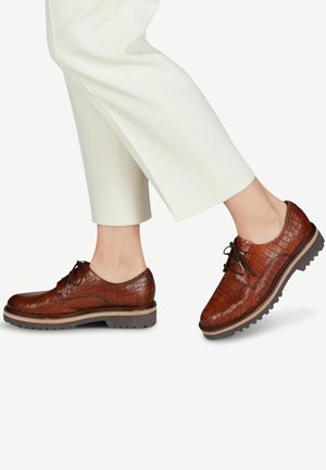 Brown leather lace-up shoes with a crocodile texture, round toe, and contrasting sole detailing. Paired with light-colored pants.