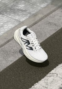 White running shoe with textured mesh upper, black detailing, and a cushioned sole. Features logo on the side and laces at the front.