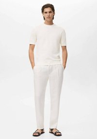 Witte, geribbelde shirt met korte mouwen, gecombineerd met lichtbeige broeken en zwarte sandalen. Eenvoudig ontwerp, ruime pasvorm, licht gestructureerde stof.