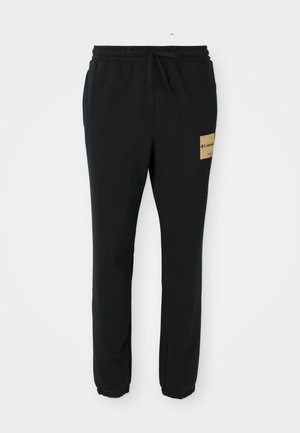 Schwarze, schmal zulaufende Sweatpants mit elastischem Bund, Kordelzug, umschlagenen Knöcheln und einem beigen Columbia-Logo-Patch am rechten Oberschenkel.