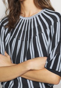 Sweter w paski w kolorze czarnym i jasnoniebieskim, z okrągłym dekoltem i teksturowanymi, pionowymi liniami. Dzianina o luźnym kroju.