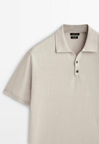 Polo beige clair à manches courtes avec deux boutons foncés et un col plié, en tissu de coton doux.