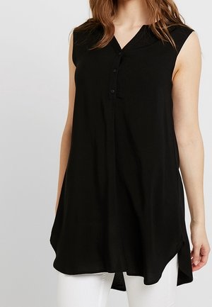 Ärmellose schwarze Tunika mit V-Ausschnitt und drei Knöpfen vorne, getragen mit weißen Hosen, abgebildet vom Hals bis zur Mitte des Oberschenkels.