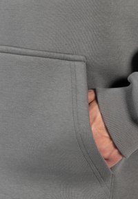 Szara bluza z kieszenią z przodu, z prążkowanymi mankietami i wyraźnymi szwami. Materiał jest gładki o miękkiej fakturze.