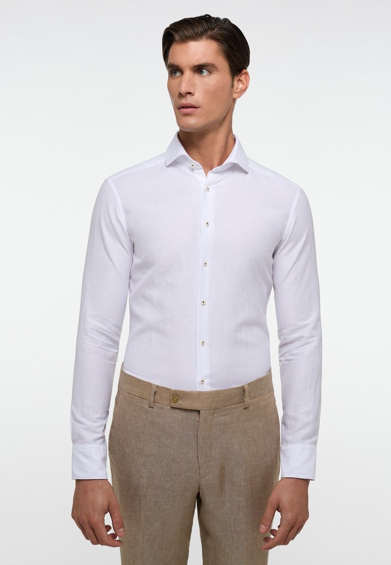 Witte langemouwen shirt met een button-down kraag en vastgemaakte voorkant, gecombineerd met beige, gemusterde broek. Glad materiaal, geen zichtbare patronen.