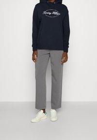 Felpa navy con logo bianco, pantaloni grigi e sneakers bianche con accenti blu. La felpa presenta un cordino e polsini a coste.