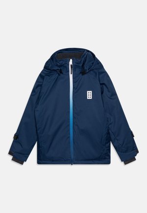 Veste à capuche bleu marine avec fermeture éclair avant présentant un dégradé blanc-bleu et un petit logo blanc sur la poitrine, affichée sur un fond blanc.