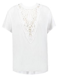 Blouse blanche à manches courtes avec détail en dentelle en forme de V présentant des motifs floraux sur le devant et un col rond.