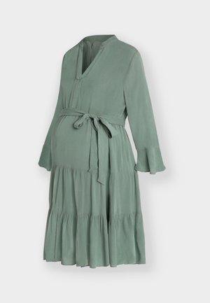 Maternitetna obleka v salvinasto zeleni barvi z V-izrezom, dolgimi razširjenimi rokavi, večplastno krilom in pasom, ki se veže.