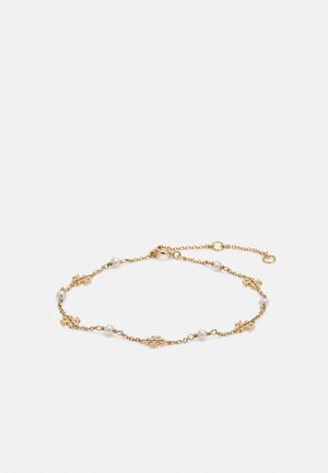 Bracelet délicat en chaîne dorée avec petites perles blanches et charms en forme de pièce de puzzle dorée, présenté sur fond blanc.