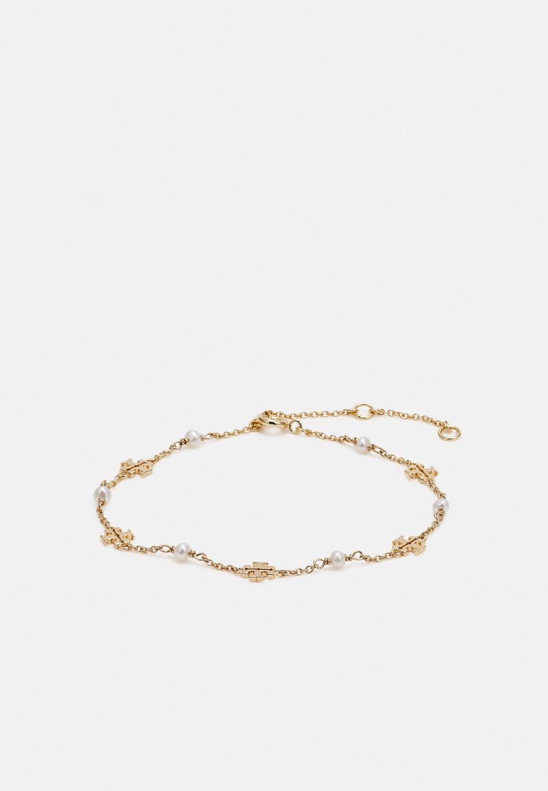 Bracelet délicat en chaîne dorée avec petites perles blanches et charms en forme de pièce de puzzle dorée, présenté sur fond blanc.