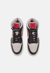 Paire de baskets montantes aux couleurs noir, gris et rouge, lacets noirs, avec un logo rouge sur la languette représentant la silhouette d’un joueur de basket.
