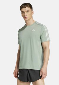 T-shirt de sport vert clair avec des manches courtes et trois bandes blanches sur les épaules. Présente un petit logo blanc sur la poitrine.