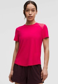 Fuchsiové športové tričko s krátkym rukávom vyrobené z ľahkej tkaniny s okrúhlym výstrihom a sieťkovými akcentmi na pleciach, skombinované s tmavými šortkami.