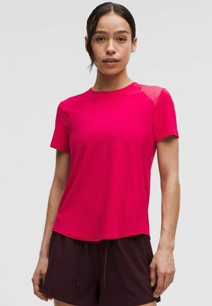 Fuchsia Sport-T-Shirt mit kurzen Ärmeln aus leichtem Stoff, Rundhalsausschnitt und Netz-Einsätzen an den Schultern, kombiniert mit dunklen Shorts.