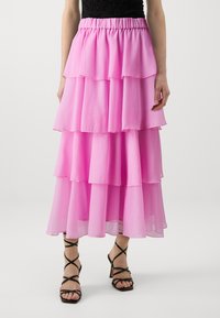 Lang, lagdelt skjørt i lys rosa chiffon med elastisk midjebånd. Kombinert med svarte høyhælte sandaler med stropper.