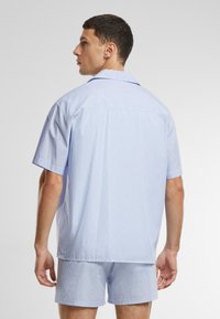 Korte mouwen pyjama set in lichtblauw met dunne witte strepen. Zachte, lichte stof; kraagdetail; shorts tot op de knie.