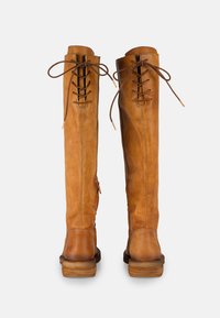 Bottes en cuir marron montantes avec un laçage à l'avant, un haut texturé et un talon en bois empilé. Détail de fermeture éclair sur le côté.