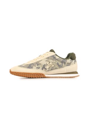 Beige en olijfgroene lage sneaker met camouflagepatroon, gestructureerde gumzool, vetersluiting aan de voorkant en logo op het zijpaneel.