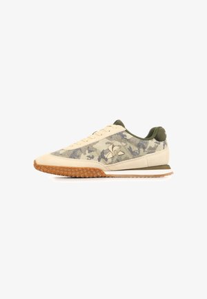 Beige en olijfgroene lage sneaker met camouflagepatroon, gestructureerde gumzool, vetersluiting aan de voorkant en logo op het zijpaneel.
