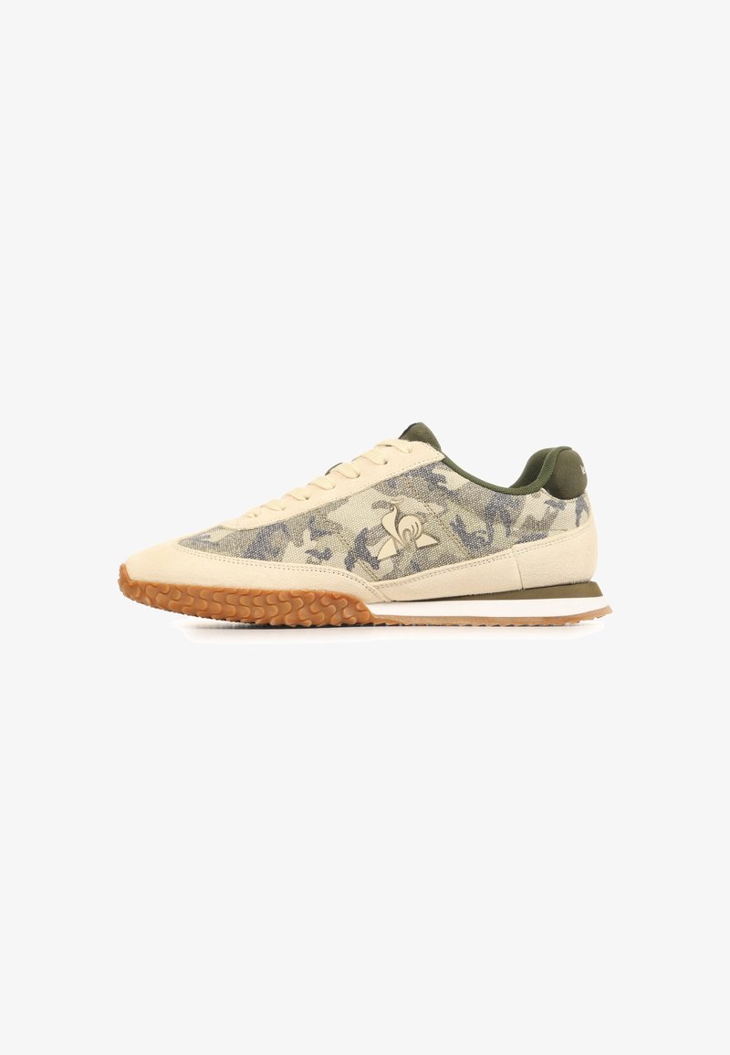 Baskets basses beige et vert olive avec motif camouflage, semelle en gomme texturée, fermeture à lacets sur le devant et logo sur le panneau latéral.