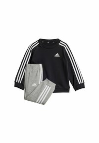 Felpa navy con strisce bianche e logo; pantaloni della tuta grigi con strisce coordinate. Tessuto morbido, collo a giro, e bottoni a pressione sulla spalla.