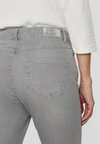 Gray denim jeans featuring a standard back pocket with a silver button and a textured waistband. Visible stitching details enhance the design.